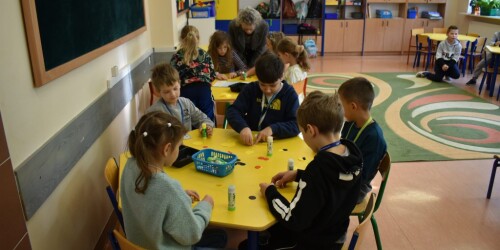 Uczniowie siedzą przy stoliku i wykonują kaczkę w stylu origami